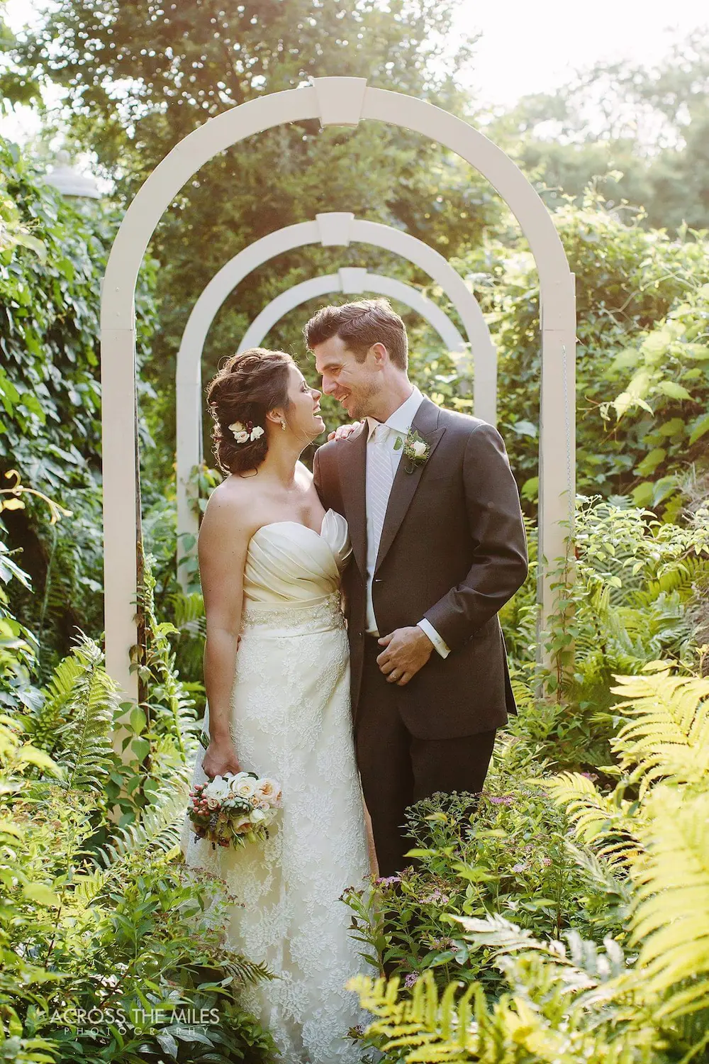 Groom in a custom charcoal suit with his bride under a garden arch