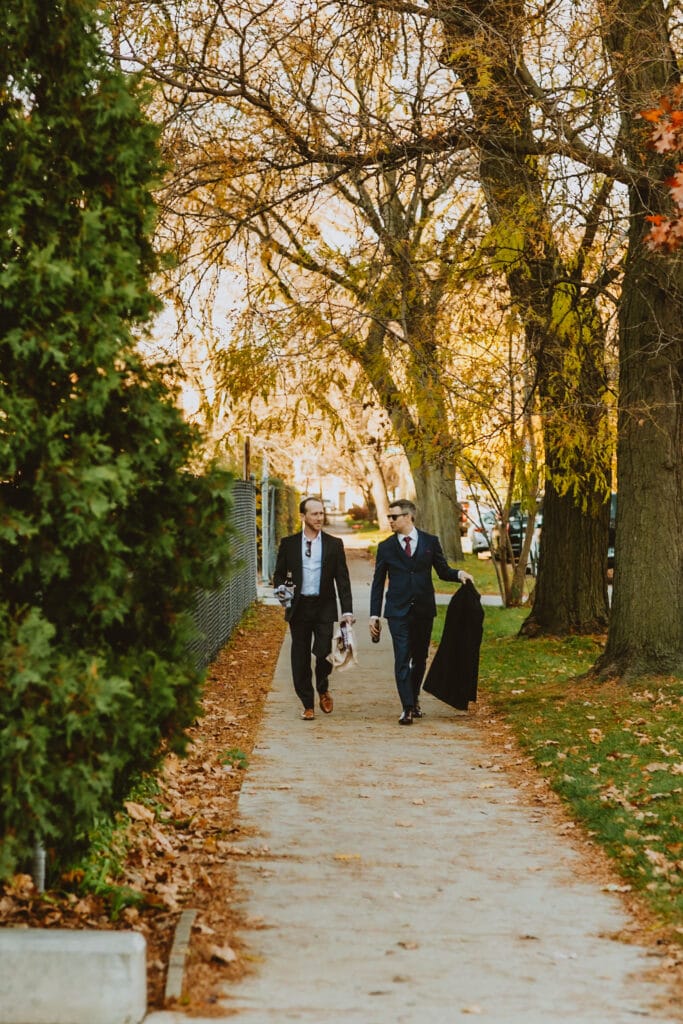 0003-20231111_0012_MN_MN_C2141 Two men walking down a pave way wearing wedding suits