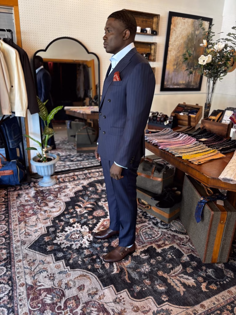WhatsApp Image 2026-05-22 at 03.53.37 Man wearing a navy pinstripe bespoke suit inside a tailoring studio
