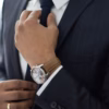 Close-up of a man adjusting his suit jacket and tie, with a wristwatch and ring visible, illustrating attention to detail in bespoke suit fitting