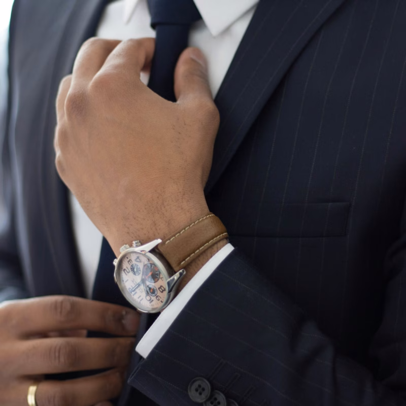 Close-up of a man adjusting his suit jacket and tie, with a wristwatch and ring visible, illustrating attention to detail in bespoke suit fitting