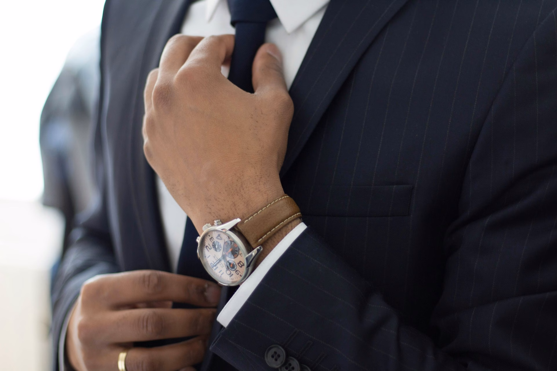 Close-up of a man adjusting his suit jacket and tie, with a wristwatch and ring visible, illustrating attention to detail in bespoke suit fitting
