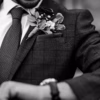 Black-and-white close-up of a man wearing a custom tailored checked suit, tie and floral boutonniere.