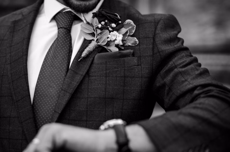 Black and white close-up of a windowpane check suit with pin dot tie, floral boutonniere and wristwatch