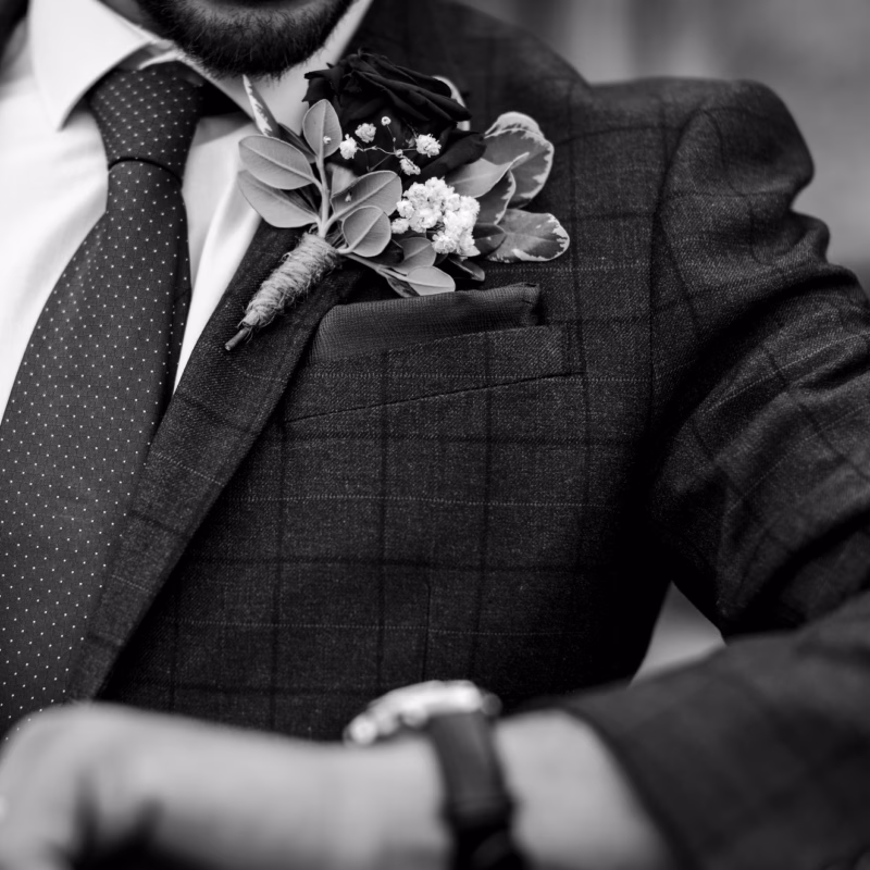 Black-and-white close-up of a man wearing a custom tailored checked suit, tie and floral boutonniere.